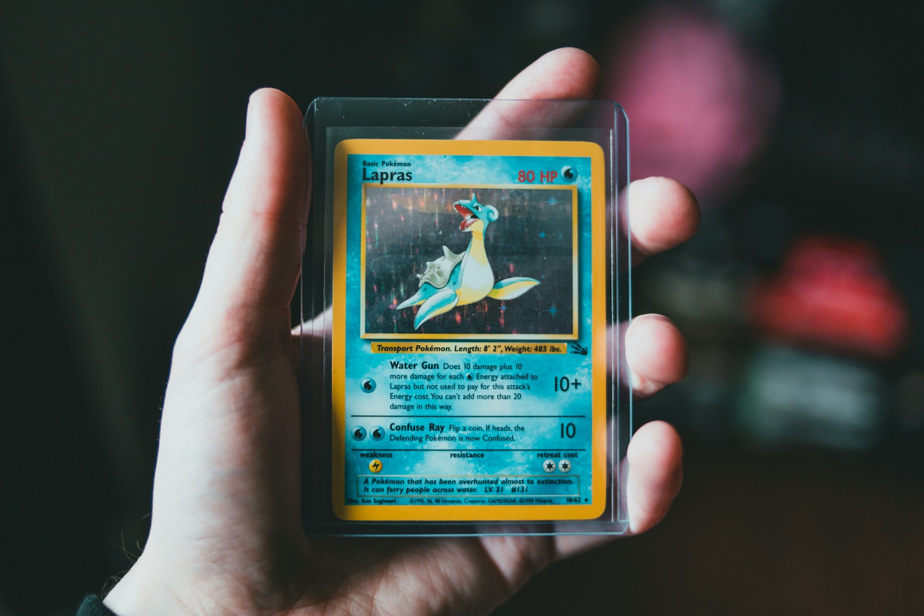 main tenant une carte Pokémon Lapras sous étui, face visible en entier