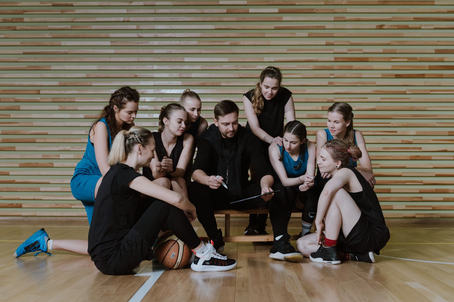 Entraîneur assis avec une équipe de basketball féminine réunie autour de lui dans un gymnase, séance de briefing