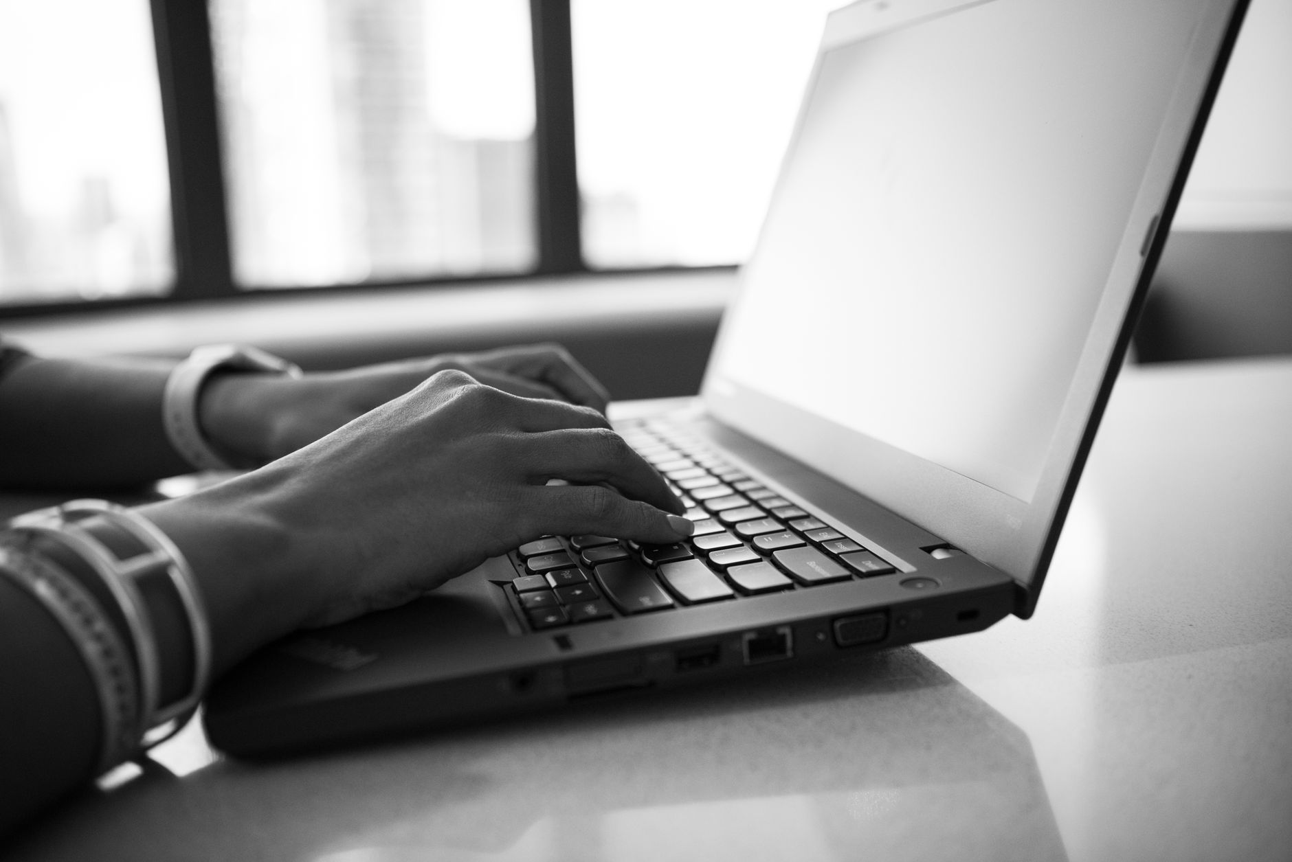 personne assise à un bureau, mains sur le clavier d'un ordinateur portable, écran affichant une interface de document