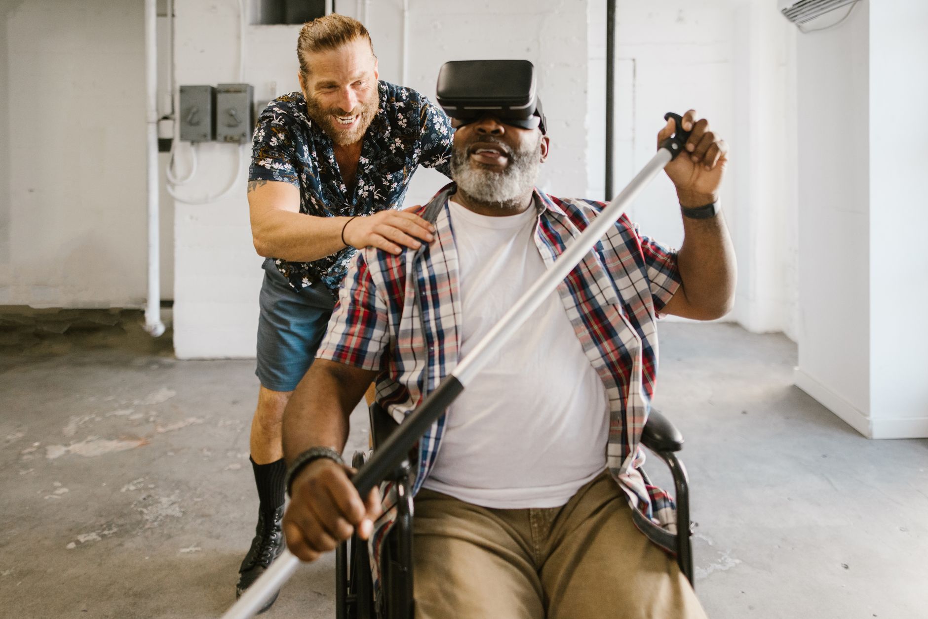 homme en fauteuil roulant portant un casque de réalité virtuelle et tenant une perche pendant un exercice, encouragé par un accompagnant