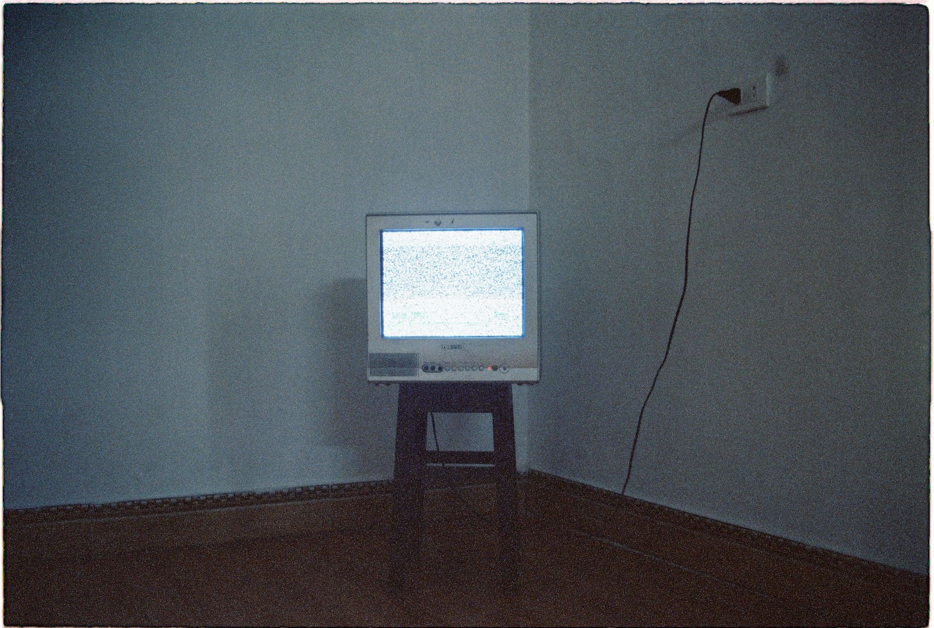 téléviseur cathodique posé sur un tabouret dans un coin de pièce, écran rempli de neige